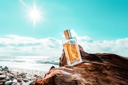 Toilet water. A rectangular glass bottle of golden perfume standing on a driftwood. Ocean waves and sunny sky in the background. Low angle view. Perfume concept and advertising template.