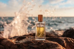 A glass perfume bottle stands on the stones, close-up. In the background is the ocean, the horizon line and the sea surf. The concept of selective perfumery.