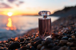 Perfumery and marketing. Lilac glass perfume bottle on a pebble beach, on the seashore, close-up. Sunset on the background. Luxury Perfume presentation concept.