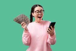 Portrait of a cheerful young woman holding money banknotes and celebrating isolated over yellow background