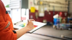 A manager is holding a pen and risk matrix form with factory workshop place as blurred background. Industrial risk assessment and safety audit concept scene. Close-up and selective focus at hand part.