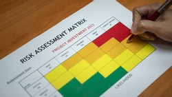 Action of a manager is using ballpoint pen to evaluate on risk assessment matrix of the Project investment 2023. Business planning working concept photo. Close-up and selective focus at hand.