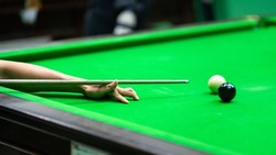 Action of a human is aiming to hitting the white snooker ball. Playing snooker activity photo, selective focus at the human's hand.