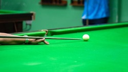Action of a human is aiming to hitting the white snooker ball. Playing snooker activity photo, selective focus at the human's hand.
