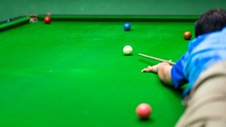 Action of a human is aiming on the white snooker ball. Playing snooker activity photo, selective focus.