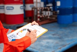 A worker is checking on the hazardous chemical material information form with background of chemical storage area at the factory place. Industrial safety working action. Selective focus.