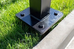 Metal pillar fastened to basement with anchor bolts and nuts. The support of the iron black pillar on a green lawn in the park