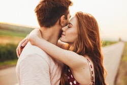 Close-up portrait of a caucasian young loving couple embracing while standing on a roadside. Couple embracing road travel. Sunset scene.