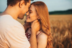 A couple touching foreheads being romantic and kissing while posing under sunlight with a blurry background. Love and relationships outdoors.