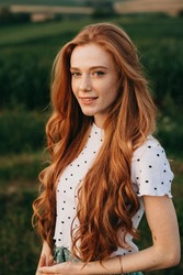 Portrait of a ginger woman with long hair, looking at camera, standing outdoors. Attractive beautiful girl. Female beauty portrait.