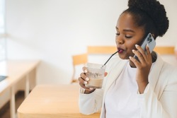 Positive afro woman having conversation on mobile phone enjoying tasty fresh drink at coffee shop. Beauty portrait. Beauty concept. Attractive beautiful