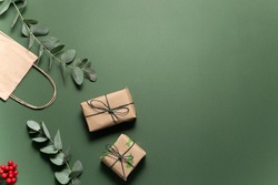 Gift boxes in craft paper and fresh eucalyptus twigs on deep green background. Christmas and New Year concept.