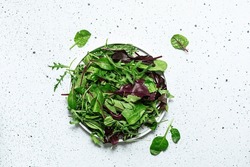 Fresh green mix of different salad leaves on white marble background top view. Healthy diet food concept.