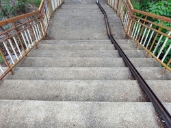 Stair-safe bike ramp along stairs. Comfortable and safe lanes for bicycles on stairs. Old and rusted steel rails for bicycles up and down for comfort between steps on stairs in the public park.
