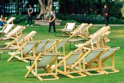 Many empty white deck chairs with tables in lawn is surrounded by shady green grass. Comfortable on outdoor patio chairs in garden.  Lawn chairs in the park. Sunbeds in the garden. Selective focus.
