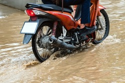 Man ride motorcycle passing through flooded road. Riding motorbike on flooded road during flood caused by torrential rains. Flooded road with large puddle. Splash by motorcycle through flood water.