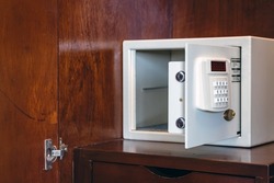 Security open metal safe with empty space inside in a wooden shelf. White safe box open door. Safe box with electronic lock in the hotel or home. Selective Focus on locking mechanism of small safes.