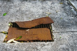 Top view of old rusted metal plate was used to cover the broken steel grating of road drain cover. Rusted steel plate cover on damaged drain grate. Sanitary sewer manhole in bad condition on the road.