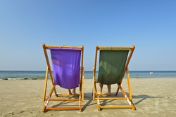 Two beach chairs stand alone on the beach facing the water.