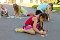 Kids absorbedly draw chalks on the pavement outdoors