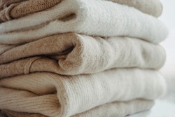 cozy milky beige and white natural wool sweaters, folded on a white background close-up. clothes made of merino wool, alpaca, natural eco-fabrics. the concept of conscious consumption. flat lay