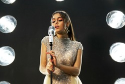 beautiful young singer in a gold dress in sequins performs on stage. girl sings into a microphone in the spotlight. artist on stage
