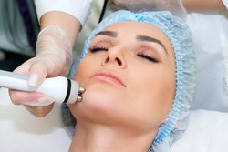 A young woman is lying on the RF-lifting procedure for face skin tightening and face contour correction. Close-up.