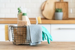 Basket with brushes, rags, natural sponges and cleaning products. Modern kitchen interior in the background. House cleaning concept
