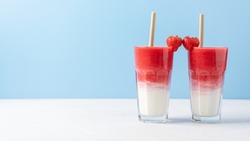 Protein rich smoothies with yogurt and frozen strawberries in glass on light blue background. Concept of drinks for lovers on Valentine's Day. Bright berry as a symbol of the heart