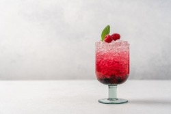 Glass of bright pink raspberry drink with crushed ice on light background. Refreshing berry summer drink