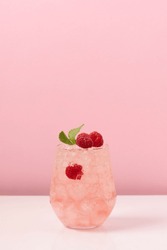 Raspberry drink with ice in glass on pink background. Refreshing tropical summer berry lemonade or alcoholic drink with raspberry berry 