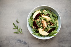 Arugula, beets, apples and nuts salad in bowl on gray background