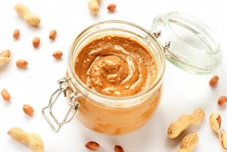Peanut butter in a jar and scattered peanuts isolated on white background