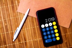 Mobile device with a calculator displaying 2019 new year on a wood table with a notebook and a pen