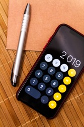 Mobile device with a calculator displaying 2019 new year on a wood table with a notebook and a pen