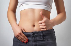 slim, athletic waist of a young woman on white background. The hand in the foreground shows a finger up gesture. the concept of female beauty and health, nutrition and diet, a beautiful figure