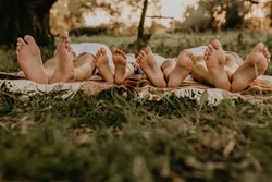 close-up bare feet of whole family resting. cheerful happy family dad mom daughters lay laying on grass picnic plaid have fun at summer outdoors together. father mother sisters parents barefoot people