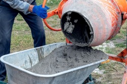 A worker pours cement mortar, concrete, from a concrete mixer into a wheelbarrow. Preparation of cement mortar at the construction site