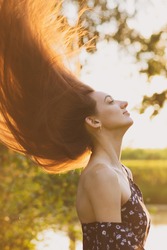 Gorgeous young brunette woman portrait with levitating hairs during golden summer sunset in blurred nature background. Image contain noise and blurred