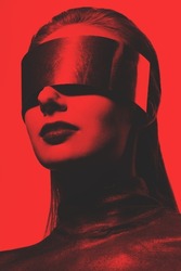 Fashion and sci-fi concept. Abstract woman studio portrait with make-up and big futuristic metallic glasses or helmet covering her eyes. Model wearing dark blouse. Toned image with red and black color