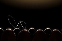 Bunny ears silhouette stick out from behind rows of eggs. Easter composition with eggs and bunny on a black background with copy space.