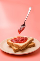a dish of toast spread with jam and a levitating spoon against a pastel pink background.
