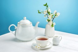 Spring composition with a teapot, a cup of tea and a blossoming cherry branch on a blue background.