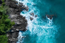 Aerial drone top view of ocean's beautiful waves crashing on the rocky island coast