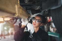 Female auto mechanic work in garage, car service technician woman check and repair customer car at automobile service center, inspecting car under body and suspension system, vehicle repair  shop.