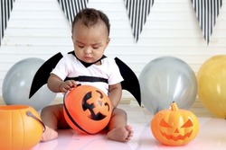 Adorable African baby kid dressing up in vampire fancy Halloween costume with black bat wings, cheerful little cute child go to party, playing trick or treat, Happy Halloween celebration.