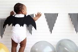 Back of adorable baby kid dressing up in vampire fancy Halloween costume with black bat wings, cheerful little cute child go to party, playing trick or treat, Happy Halloween celebration.