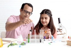 Cute Indian school girl in India traditional dress costume doing science experiments in laboratory with father or teacher tutor, young scientist kid with lab equipment learning chemistry in classroom.