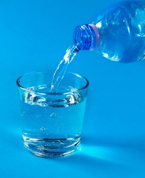 Pouring water from a bottle into a glass in a blue colors design. Refreshment drinking water, dieting and health care beverage.