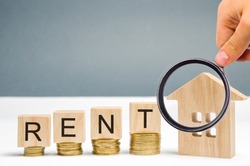 Magnifying glass, wooden blocks with the word Rent, coins and a miniature house. The concept of renting housing and real estate. The cost of a rented home or apartment. Saving money. Rental.